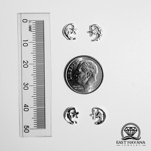 May include: Four silver crescent moon and star earrings, shown next to a US dime for size comparison. The earrings are small and delicate, with a simple design.