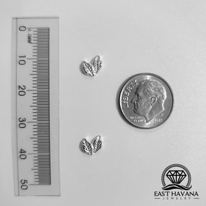 May include: Two silver leaf charms, each with two leaves, are shown next to a US dime for size comparison. The charms are small and delicate, perfect for adding a touch of nature to jewelry.
