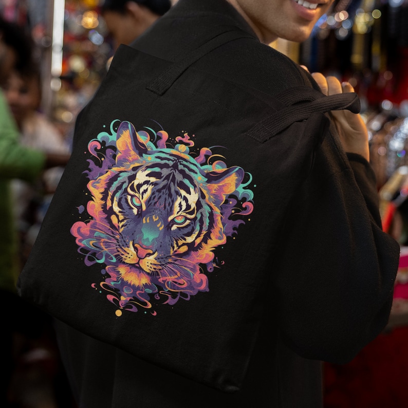 K&ouml;nnte beinhalten: Eine schwarze Canvas-Tragetasche mit einem bunten Tigerkopf-Motiv. Das Gesicht des Tigers ist von Wirbeln in Rosa, Lila, Blau und Gelb umgeben.