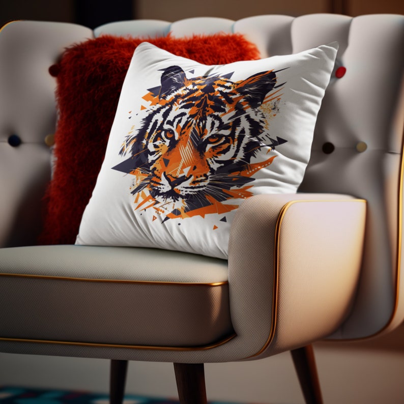 K&ouml;nnte beinhalten: Ein wei&szlig;es Kissen mit einem farbenfrohen, abstrakten Tigergesichtsdesign. Das Kissen liegt auf einem hellgrauen Sessel mit einem roten Kissen.
