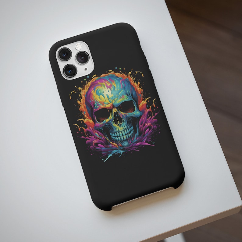 May include: A black phone case featuring a colourful skull graphic. The skull is surrounded by splashes of paint in shades of blue, purple, pink and yellow.