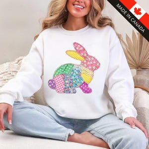 May include: White sweatshirt with a patchwork bunny design. The bunny is made from various patterned fabrics, including floral, polka dot, and gingham. The sweatshirt has long sleeves and a crew neck. "MADE IN CANADA" is printed on the upper right corner.
