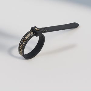 May include: Black ring sizer tool with gold lettering and markings. The tool has a flat, rectangular handle extending from the ring portion. The ring portion has letters and numbers printed on it. The tool is used to measure ring sizes.