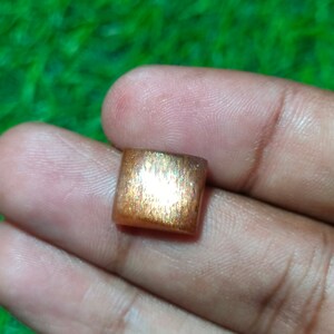 Op de afbeelding: Een vierkante, iriserende sunstone edelsteen met een goudbruine kleur en een glinsterende, metallic glans.
