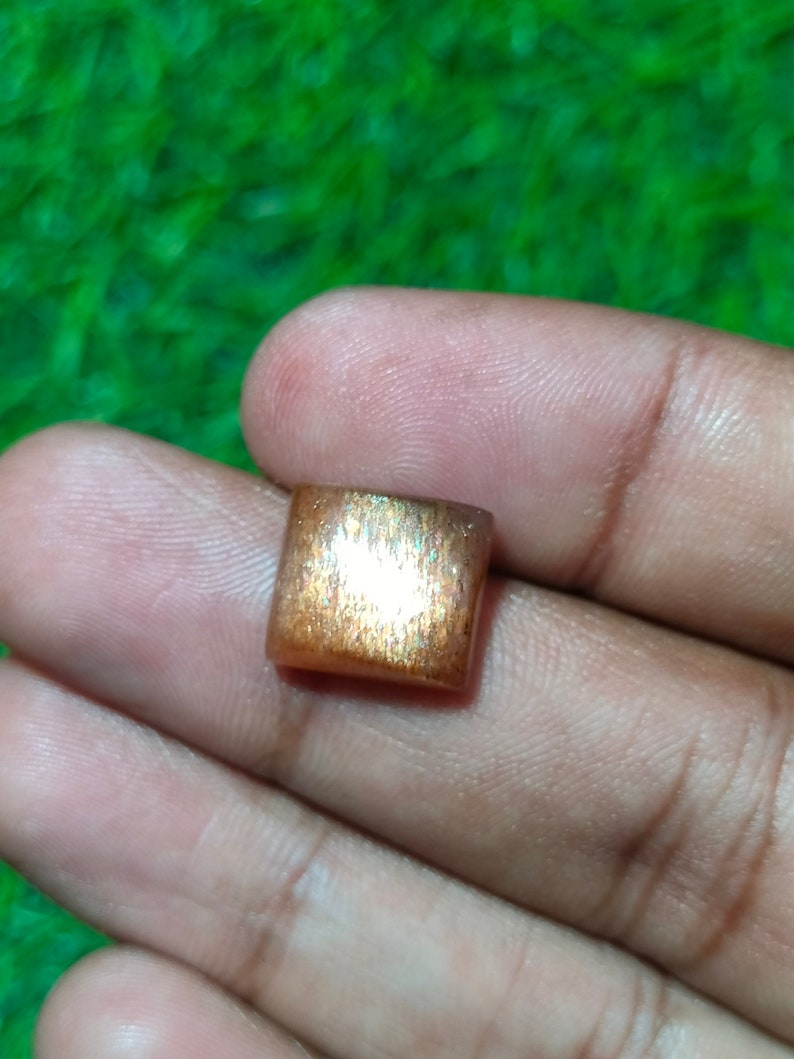 Op de afbeelding: Een vierkante, iriserende sunstone edelsteen met een goudbruine kleur en een glinsterende, metallic glans.