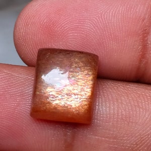 Op de afbeelding: Een vierkante, iriserende zonnesteen edelsteen met een roodbruine kleur en een glinsterende, glimmende afwerking.