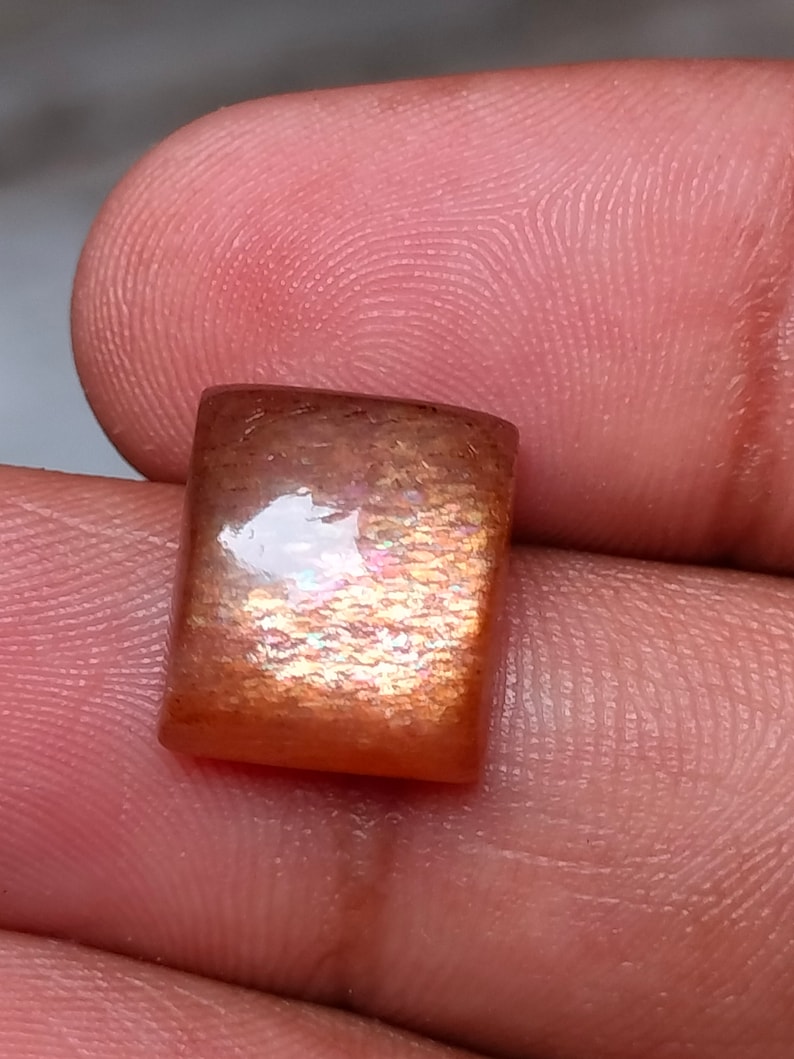 Op de afbeelding: Een vierkante, iriserende zonnesteen edelsteen met een roodbruine kleur en een glinsterende, glimmende afwerking.