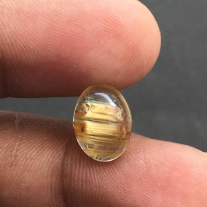 以下が含まれることがあります： 金色がかった茶色の縞模様と内包物を含む、透明な楕円形の宝石。宝石の長さは約2.5cmです。