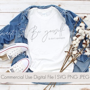 Puede incluir: Camiseta blanca con el texto "Be yourself & don't apologize" en fuente de letra cursiva negra. La camiseta está colocada sobre una superficie de madera con una chaqueta vaquera, zapatillas blancas y tallos de algodón.