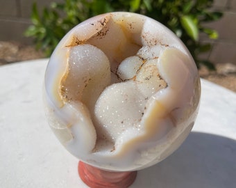 May include: A white agate geode sphere with brown and white crystals inside. The sphere is sitting on a wooden base.