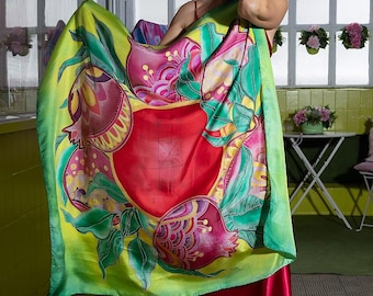Puede incluir: Un vibrante pañuelo de seda con un diseño de granada en tonos rojos, rosas, verdes y amarillos. El pañuelo se muestra, destacando la intrincada obra de arte. El fondo incluye a una mujer con un vestido rojo.