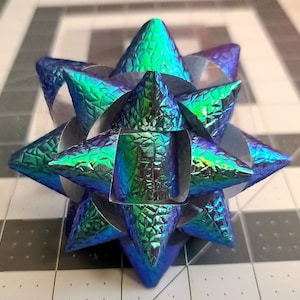 May include: A blue and green iridescent bow with a starburst shape. The bow is made of a textured material and has a shiny finish.