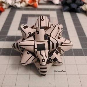 May include: A white and black patterned bow with a circuit board design. The bow is folded into a star shape.