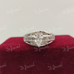 Peut inclure: Une bague en argent avec un grand diamant de forme marquise entouré de diamants plus petits. La bague est posée sur un fond de velours rouge.