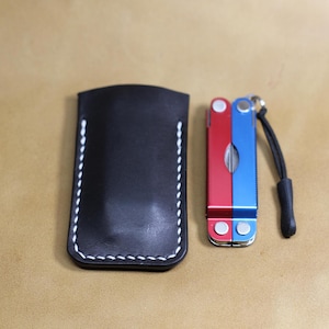 May include: A white ceramic mug with a black handle and the text "But First, Coffee" in a black, handwritten-style font. The mug is on a white surface.