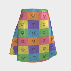 May include: A colorful, knee-length skirt featuring a patchwork design of squares in various colors, including yellow, pink, orange, green, and purple. Each square has a repeating bear face pattern. The skirt has a flared silhouette.