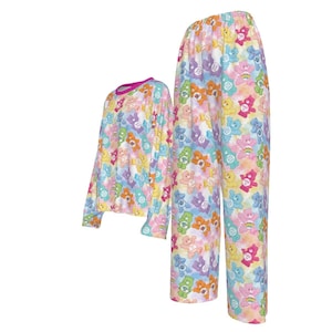 K&ouml;nnte beinhalten: Ein zweiteiliger Schlafanzug mit einem sich wiederholenden Muster aus bunten Zeichentrickb&auml;ren. Das lang&auml;rmlige Oberteil hat einen rosa Ausschnitt und Manschetten. Die passende Hose hat eine lockere Passform. Der Schlafanzug ist aus weichem, leichtem Stoff.