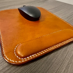May include: A brown leather mouse pad with a wrist rest and white stitching. A black wireless mouse is on the pad.