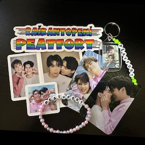 May include: A collection of fan merchandise featuring photos of two men, including a keychain with a clear plastic charm, a bracelet with the words "PEATFORT" and a heart, and stickers with the text "RAIKANTOPENI" and "PEATFORT".