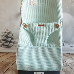 May include: A light green waffle weave fabric baby chair cover with a brown leather tag that says "ByB Atelier". The cover is on a black base with the BumBo logo.