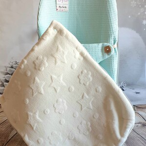 May include: A light blue waffle weave baby chair cover with a white plush blanket with a star and flower pattern. The blanket is folded and placed inside the chair cover. The chair cover has a tag that says "ByB Gardez y Balance Atelier".