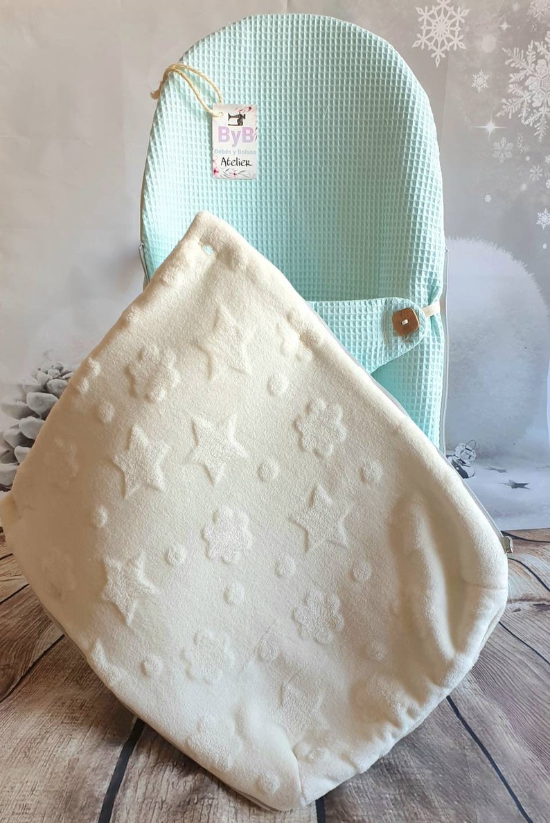 May include: A light blue waffle weave baby chair cover with a white plush blanket with a star and flower pattern. The blanket is folded and placed inside the chair cover. The chair cover has a tag that says "ByB Gardez y Balance Atelier".