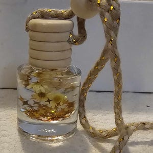 May include: A clear glass bottle with a white wooden lid and a beige rope with gold accents. The bottle contains dried flowers and gold glitter.