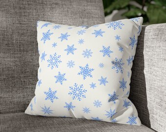May include: A white throw pillow with a blue snowflake pattern. The pillow is sitting on a gray couch.
