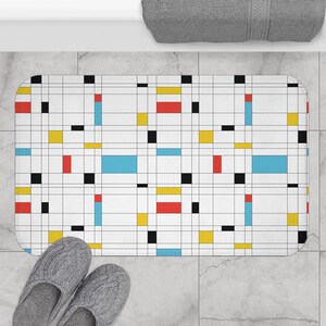 May include: A white bath mat with a geometric pattern of black, red, yellow, and blue squares. The mat is on a tiled floor.