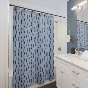 May include: A blue shower curtain with a black wavy line pattern. The curtain is hanging in a bathroom with a white vanity and a white tiled shower.