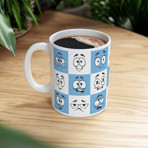 May include: White ceramic mug with a blue and white checkered pattern. Each square features a cartoon face with different expressions.
