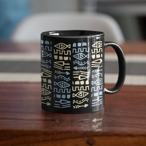 May include: Black ceramic coffee mug with a geometric pattern in shades of blue, yellow, and white. The pattern features stylized fish, arrows, and other abstract shapes.