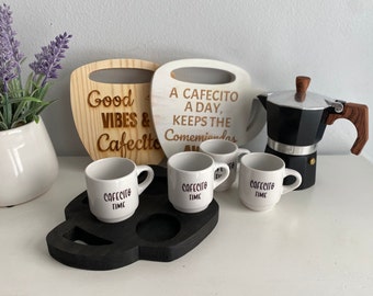 May include: A set of four white espresso cups with the text "Cafecito Time" on each cup. The cups are on a black wooden tray. There are two wooden signs with coffee-themed text, and a black and silver stovetop espresso maker.