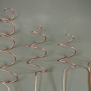 Può includere: Quattro spirali di filo di rame di dimensioni diverse. Le spirali sono avvolte e si ergono su uno sfondo grigio.