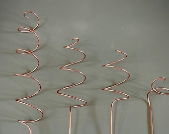 May include: Four copper wire spirals of varying sizes. The spirals are coiled and stand upright on a gray background.