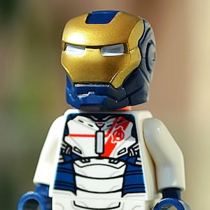 May include: A white, blue and red Lego minifigure of Iron Man wearing a helmet with a gold faceplate. The minifigure has red legs and is standing on a reflective surface.