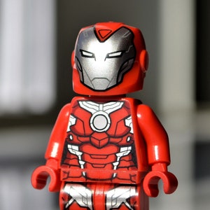 May include: A red and silver Lego minifigure of Iron Man. The figure has a red torso with silver accents and a red helmet with a silver faceplate.