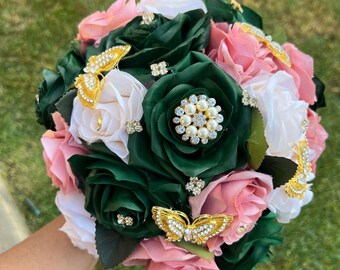 May include: A bouquet of artificial flowers in shades of pink, white, and green. The bouquet is decorated with gold butterfly brooches and pearl accents.