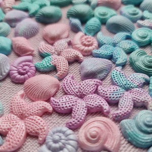 May include: A collection of pastel-colored seashell and starfish decorations. The assortment includes various shapes and sizes, with colors ranging from pink and lavender to teal and light blue. These decorative elements are ideal for crafts or coastal-themed decor.