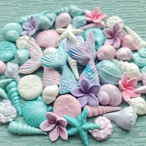 Puede incluir: Una colección de decoraciones para pasteles de cola de sirena y conchas marinas de color pastel. Las decoraciones están hechas de fondant y presentan una variedad de colores, incluyendo rosa, azul, morado y blanco.