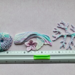 May include: A set of five pastel-colored resin sea life ornaments. The set includes a mermaid tail, a coral branch, a seashell, a flower, and a coral reef. The ornaments are approximately 2-3 inches in size.