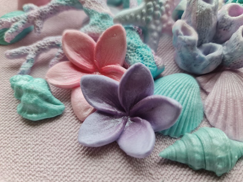 May include: A collection of pastel-colored seashells, coral, and flowers. The shells are in shades of blue and green, the coral is light blue, and the flowers are pink and purple.