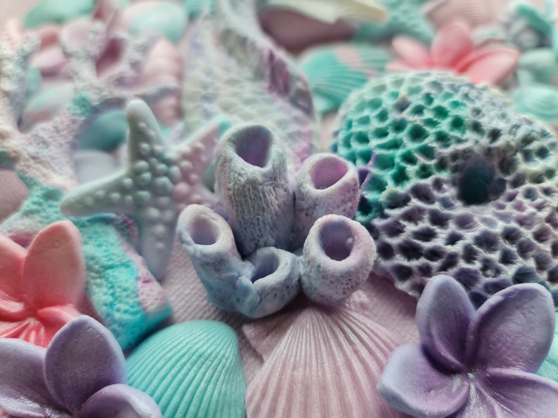 May include: A close-up of a variety of pastel-colored sea-themed decorations, including starfish, coral, seashells, and flowers. The decorations are made of a soft, textured material and have a whimsical, beachy feel.