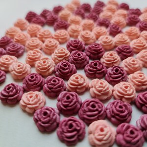 Könnte beinhalten: Eine Sammlung von Zuckerblumen-Dekorationen in Rosa und Burgunderrot, die in einem Halbkreis angeordnet sind. Die Blumen sind alle gleich groß und gleich geformt und haben ein zartes, realistisches Aussehen.