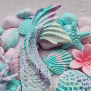 May include: A mermaid tail made of pastel blue, purple, and white resin with a shimmery finish. The tail is surrounded by various sea-themed decorations, including seashells, starfish, and coral.