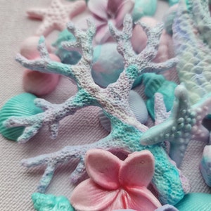 May include: A close-up of a collection of pastel-colored sea-themed decorations, including starfish, seashells, and coral. The decorations are made of a soft, textured material and have a delicate, whimsical feel.