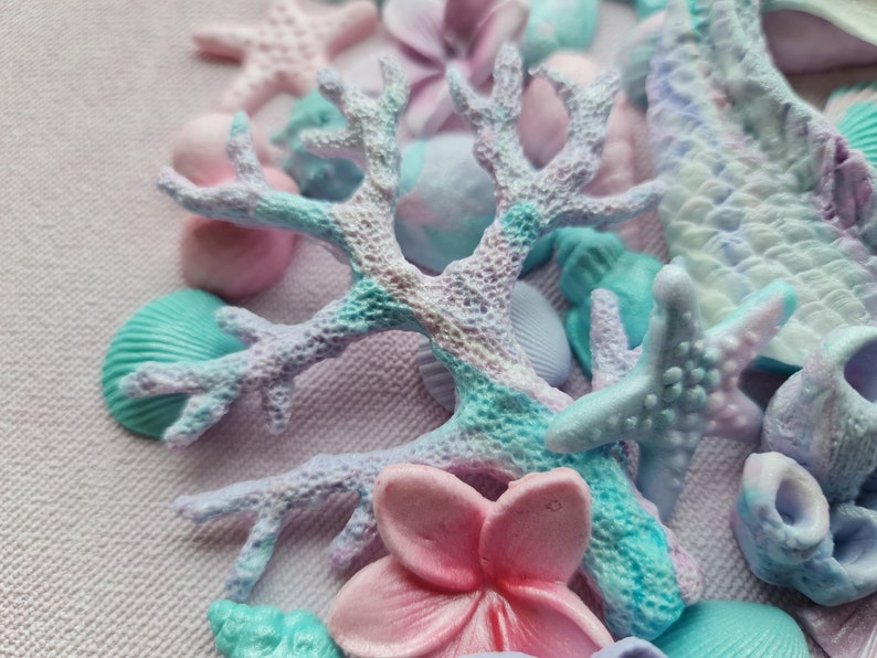 May include: A close-up of a collection of pastel-colored sea-themed decorations, including starfish, seashells, and coral. The decorations are made of a soft, textured material and have a delicate, whimsical feel.
