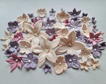 May include: Assortment of pastel-colored sugar flowers in shades of pink, purple, and cream. The flowers are made of fondant and have a delicate, realistic appearance.