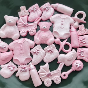 May include: Pink and white baby shower cake toppers. The set includes a baby bottle, a rattle, a baby carriage, a pair of booties, a teddy bear, a baby onesie, a dummy, and a set of blocks that spell "BIG".
