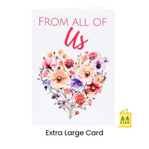 以下が含まれることがあります： ピンク色の「FROM ALL OF US」という文字が書かれた白いグリーティングカード。「Us」の文字は筆記体です。中央には、色とりどりの花で作られたハート型のフラワーアレンジメントがあります。カードには「Extra Large Card」と「A4 size」と書かれています。